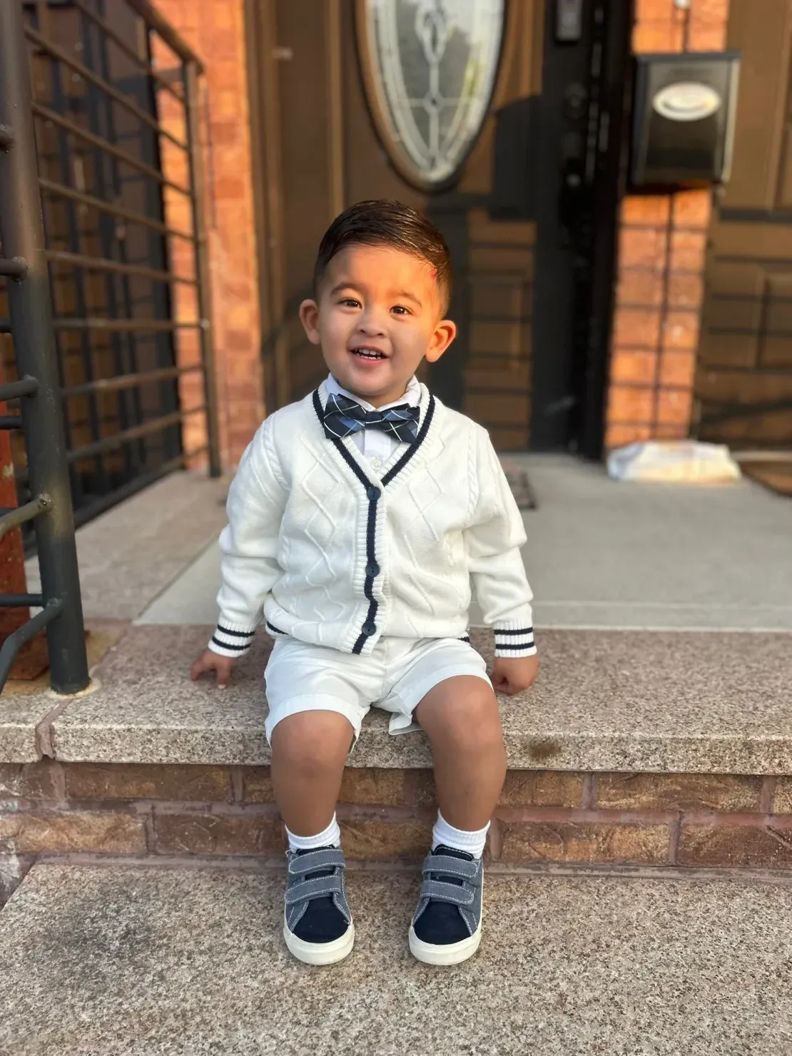 Smiling toddler in bow tie outside house