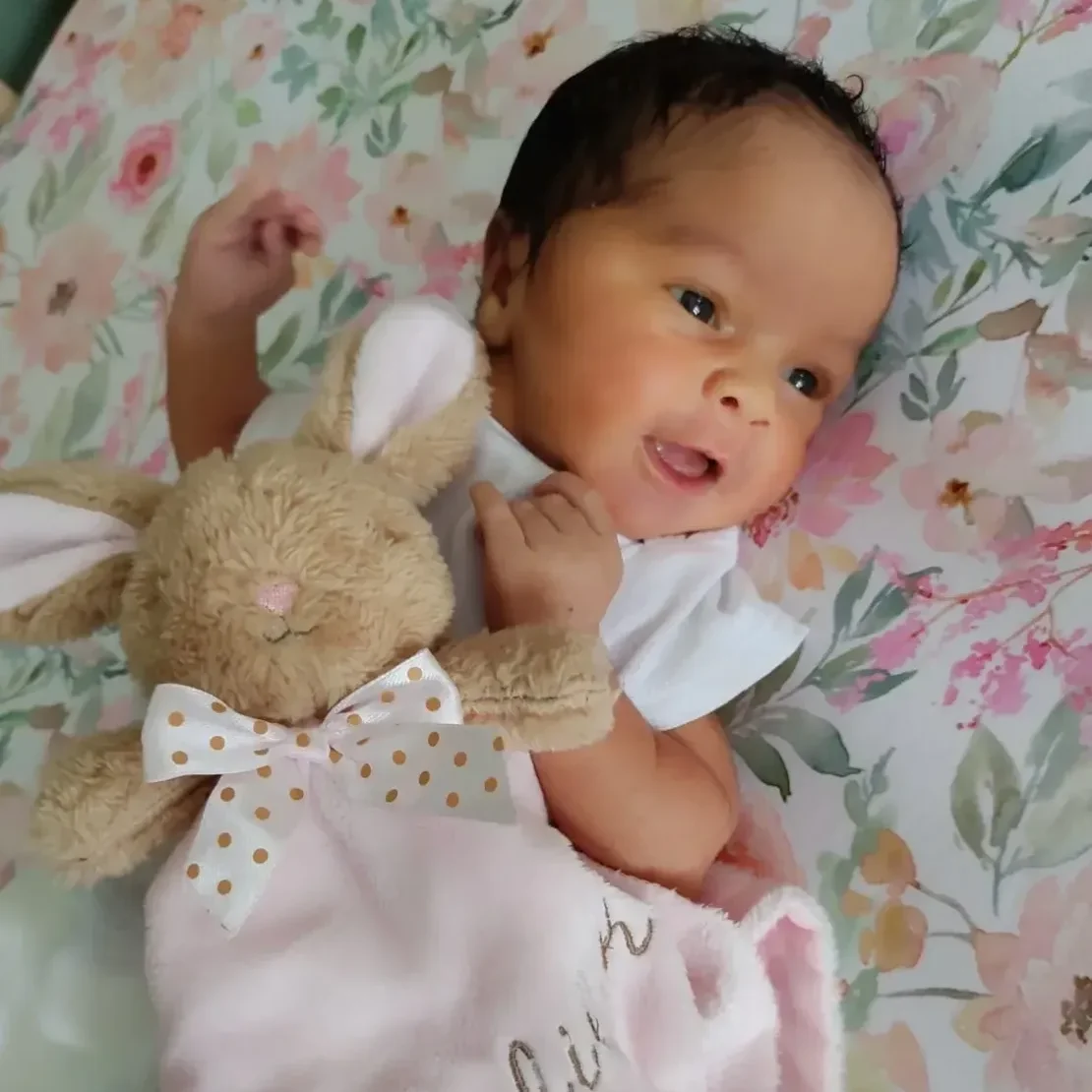 Baby with plush bunny on floral blanket